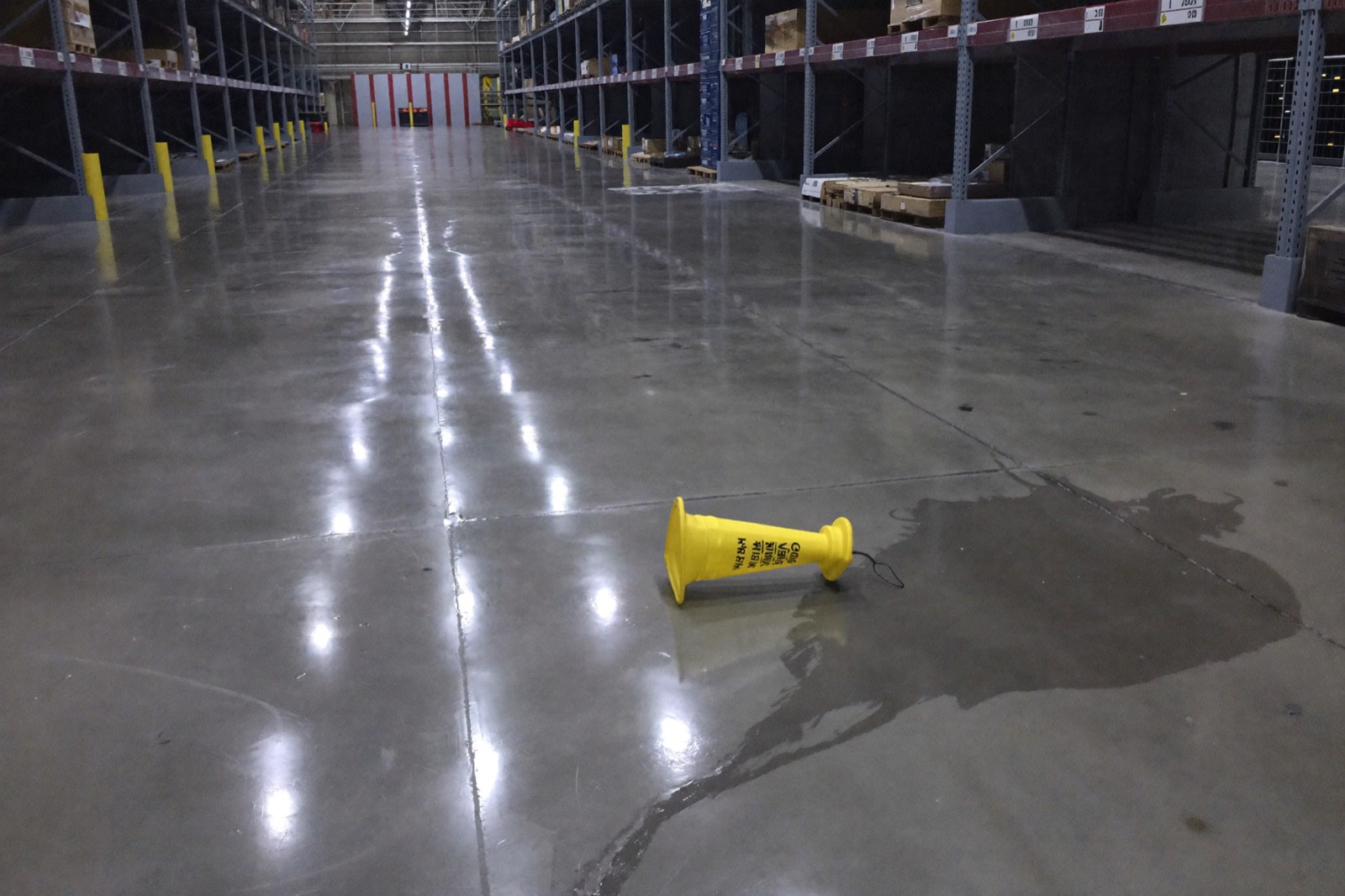 A long empty store aisle with a wet floor and a caution cone lying on its side
