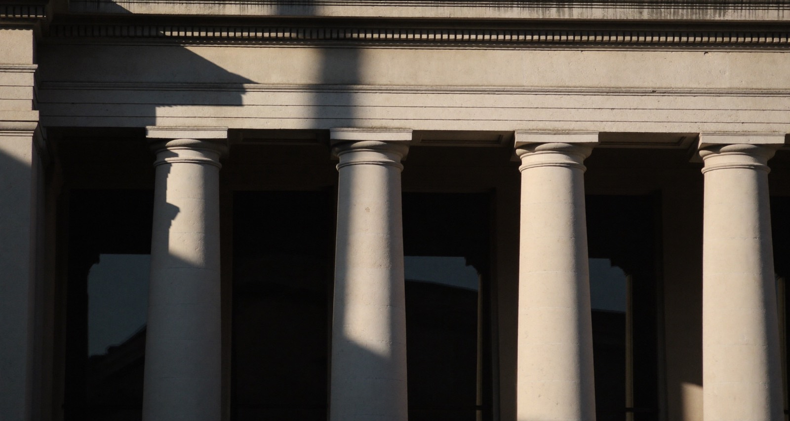 Sunlight and deep shadow across the limestone piers of a civic building